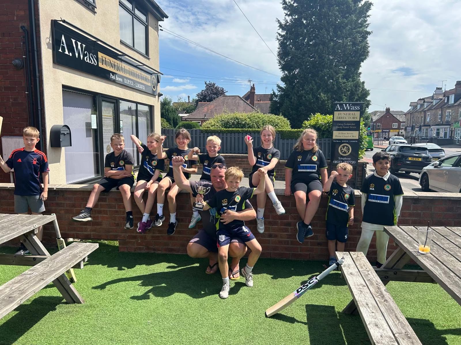 Kwik cricket team sat on a wall celebrating victory with a trophy
